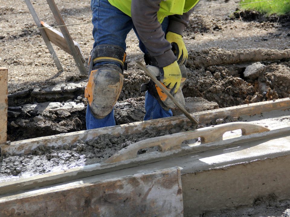 Worker wearing safety boots and leg protection on construction site.