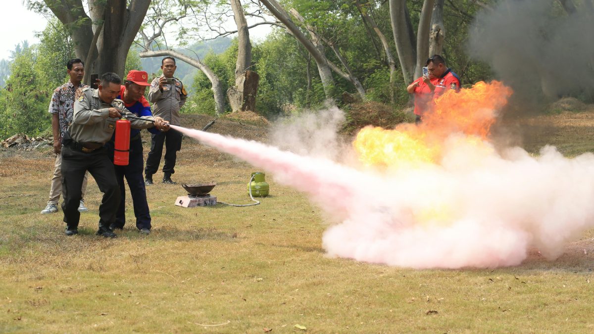 Employees receiving fire safety training using a fire extinguisher during an emergency drill.